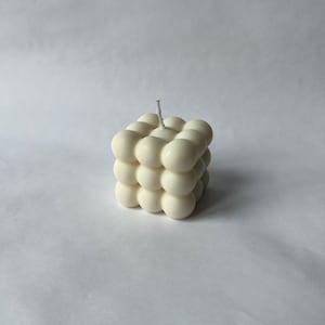 Può includere: Una candela bianca con un design rotondo e a forma di bolle. La candela ha la forma di un cubo e ha un solo stoppino.