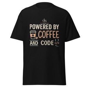 Könnte beinhalten: Ein schwarzes Kurzarm-T-Shirt mit einem Grafikdesign und dem Text "POWERED BY COFFEE AND CODE". Das Design enthält ein Kaffeetassen-Symbol, Dampflinien und Programmier-Klammersymbole in hellbraunen und blauen Farben auf der Brust.