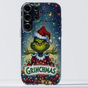 Könnte beinhalten: Eine Handyhülle mit einem Cartoon-Grinch-Charakter, der einen Weihnachtsmannhut und ein rotes Outfit trägt. Der Grinch ist von Weihnachtslichtern umgeben, darunter das Wort "GRINCHMAS". Der Hintergrund hat einen Schneeeffekt.