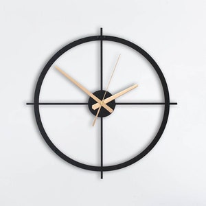 Puede incluir: Un reloj negro y dorado con un marco circular y cuatro radios. El reloj está colgado en una pared blanca sobre un sofá beige con almohadas de color turquesa y una manta de lana verde. Un sillón azul con un cojín a rayas está en primer plano. Una lámpara colgante de mimbre cuelga del techo.