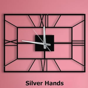 May include: A black metal wall clock with Roman numeral markings and silver hands. The clock is hanging on a pink wall above a gray couch. The text "Silver Hands" is printed below the clock.