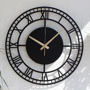 Könnte beinhalten: Schwarze, runde Wanduhr mit römischen Ziffern. Die Uhr hat ein schwarzes Zifferblatt und einen dekorativen Außenring mit römischen Ziffern. Die Zeiger sind hellbraun. Die Uhr ist an einer weißen Ziegelmauer befestigt.