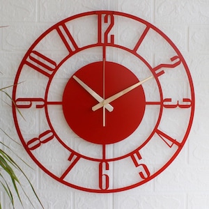 May include: A red, circular wall clock with a minimalist design. The clock has a red face with a circular centre and a cut-out frame with Roman numerals. The hands are light brown. The clock is mounted on a white brick wall.