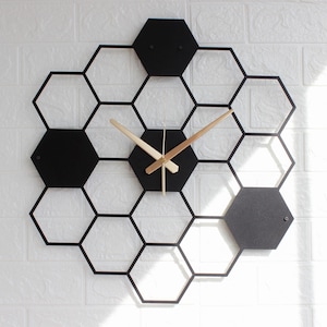 May include: A contemporary wall clock with a honeycomb design. The clock has a black frame with black hexagonal elements and gold-coloured hands. It is mounted on a white brick wall.
