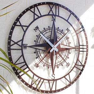 Peut inclure: Une horloge murale en métal brun avec des chiffres romains et un design de boussole. L'horloge a des aiguilles blanches et une aiguille de boussole blanche.
