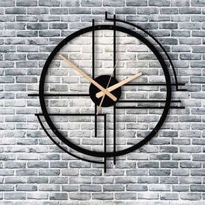 Black modern metal wall clock with gold hands without numbers on a gray rustic wall.
