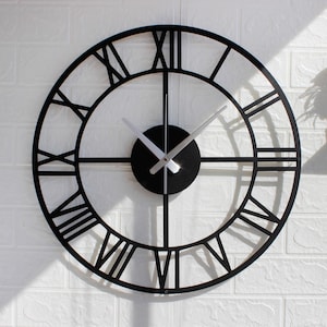 May include: A black, circular wall clock featuring Roman numerals. The clock has a minimalist design with a black face and silver hands. The clock is mounted on a white brick wall.