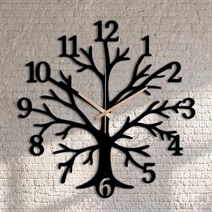 Könnte beinhalten: Eine große schwarze Wanduhr in Form eines Baumes mit weit verzweigten Ästen und Wurzeln. Die Uhr verfügt über schwarze arabische Ziffern von 1 bis 12, die in die Astspitzen integriert sind, sowie zwei dünne, helle Metallzeiger am Stamm.