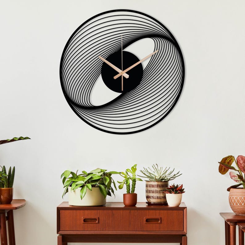 May include: A modern, black and gold wall clock with a unique, abstract design. The clock features a black circular center with gold-colored hands and a swirling, layered pattern around the perimeter. The clock is mounted on a white wall.