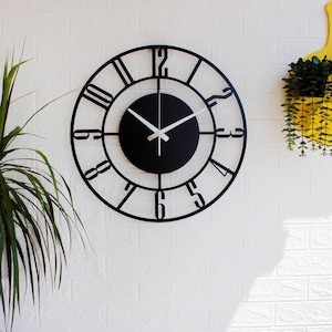 A black metal wall clock with Roman numeral markings and a black face. The clock has white hands and a simple design.