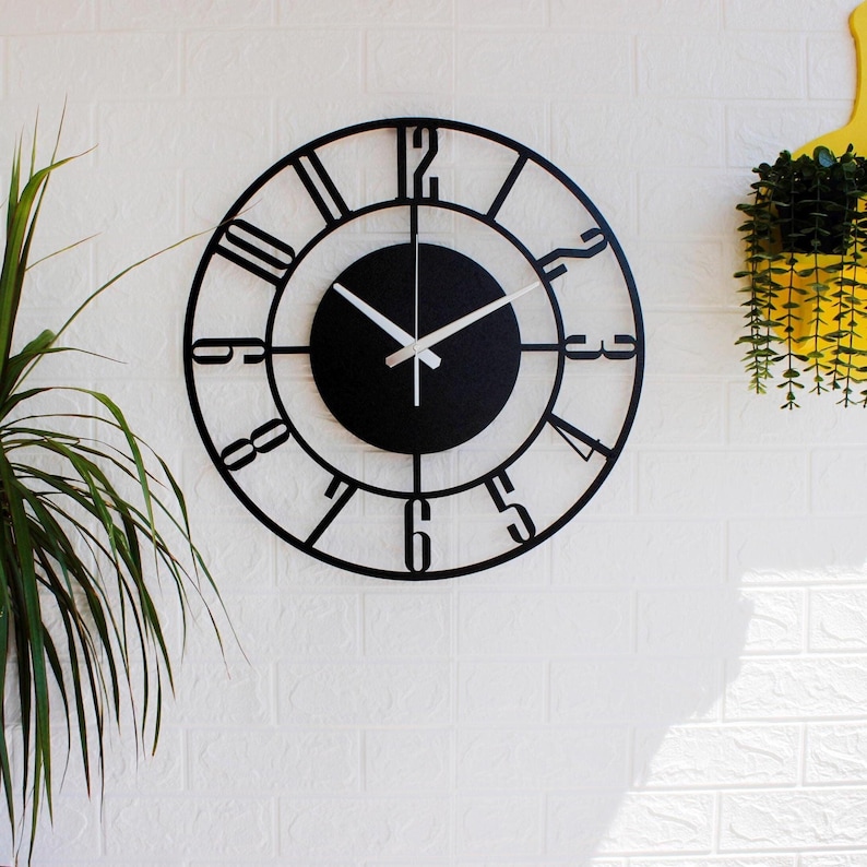 A black metal wall clock with Roman numeral markings and a black face. The clock has white hands and a simple design.