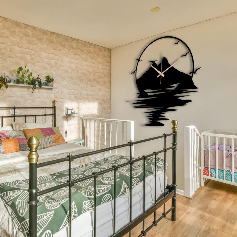 May include: A black circular wall clock featuring a silhouette of a mountain range and birds in flight. The clock face has thin, light-colored hands centered over the mountain design, which extends downward with a reflection-like pattern.