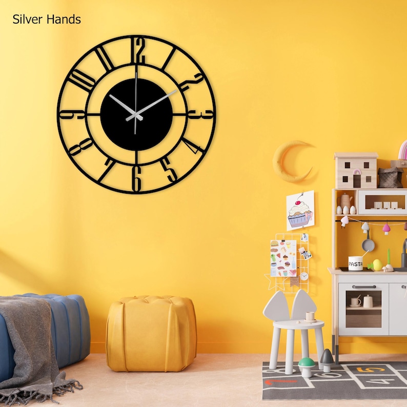 A black clock with silver hands and Roman numerals on a yellow wall. The clock is hanging above a toy kitchen with a colourful alphabet chart and a toy stove.