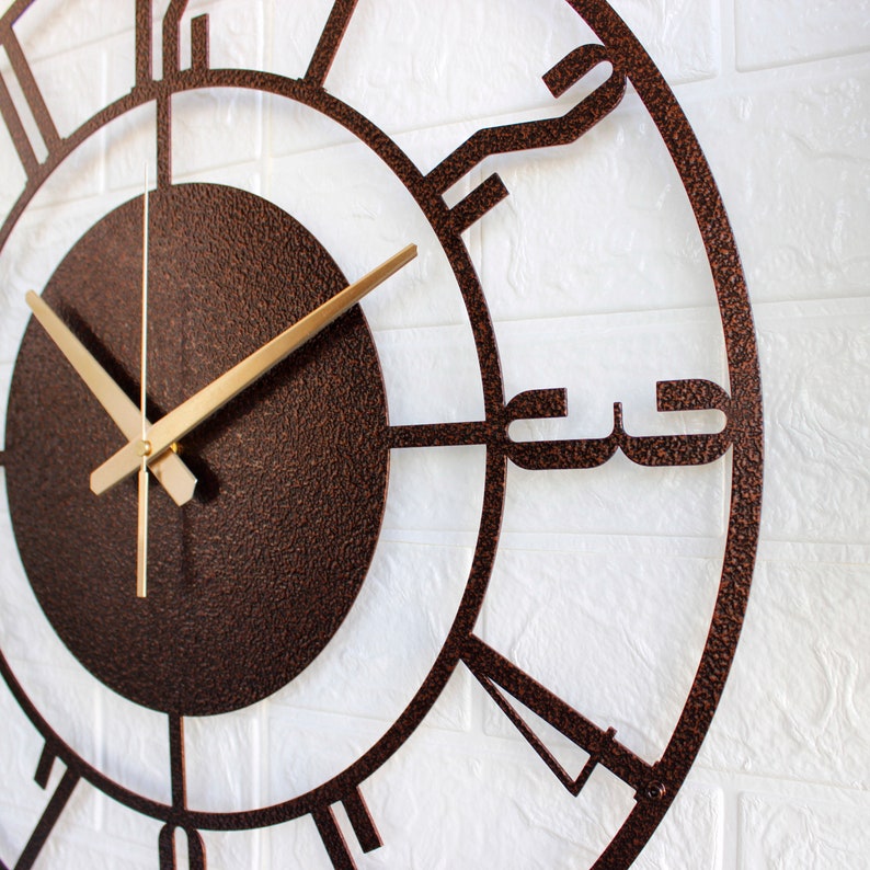 K&ouml;nnte beinhalten: Eine gro&szlig;e, runde Wanduhr aus Metall mit r&ouml;mischen Ziffern. Die Uhr hat ein braunes, strukturiertes Zifferblatt und goldfarbene Zeiger.