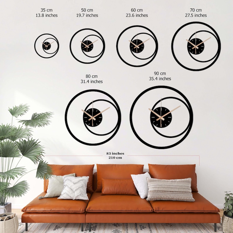 Pu&ograve; includere: Una collezione di orologi da parete neri moderni di varie dimensioni, da 35 cm a 90 cm di diametro. Ogni orologio presenta un quadrante nero con lancette chiare e un design unico a doppio cerchio. Gli orologi sono esposti su una parete bianca sopra un divano in pelle marrone.