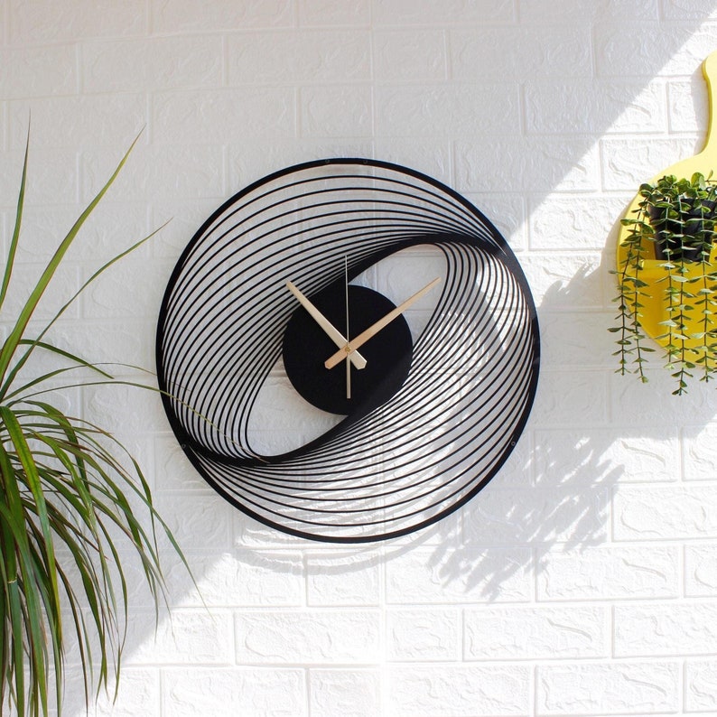 Modern spiral metal wall clock hanging on a white wall, black color, gold hand, unnumbered, interior designed with black lines.