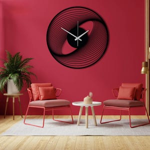 May include: Black, modern wall clock with a unique, abstract design. The clock features a circular frame with swirling lines and white clock hands. The clock is mounted on a red wall.