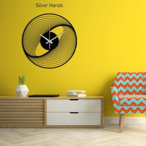 May include: A modern wall clock with a black circular design and silver hands. The clock features a unique pattern of curved lines and a black center. The text "Silver Hands" is above the clock.