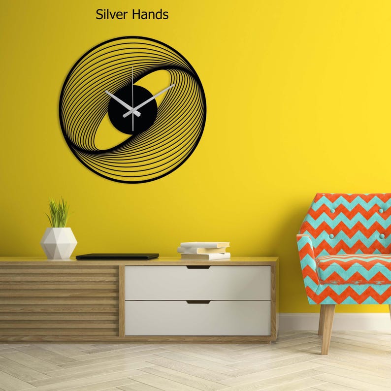 May include: A modern wall clock with a black circular design and silver hands. The clock features a unique pattern of curved lines and a black center. The text "Silver Hands" is above the clock.