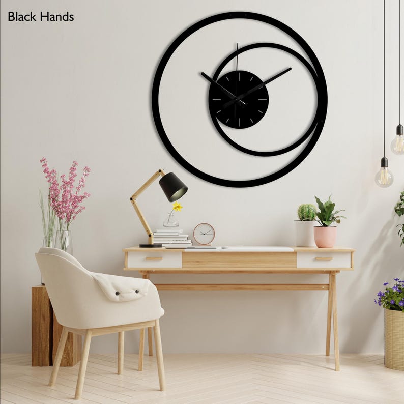 Pu&ograve; includere: Un moderno orologio da parete nero dal design unico. L'orologio presenta una cornice circolare con un cerchio pi&ugrave; piccolo e sovrapposto e un quadrante nero. Le lancette sono nere e l'orologio &egrave; montato su una parete bianca.
