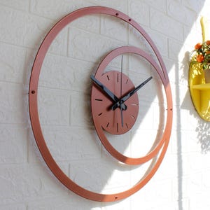 May include: A contemporary wall clock featuring a copper-toned spiral design. The circular clock face has black hands and minute markers. The spiral frame is fixed to the wall with small screws. This clock is a decorative item for home decor, measuring approximately 30 cm in diameter.