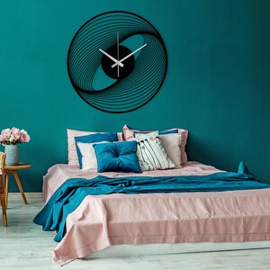 Silent, modern, spiral metal wall clock with silver hands, hanging on the blue wall, in the bedroom.