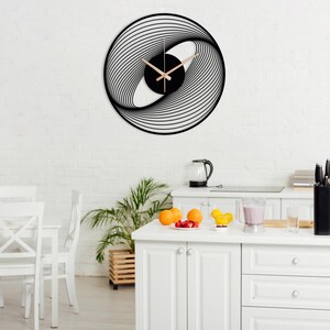 May include: A modern, black and white wall clock with a unique, swirling design. The clock face features a black center with light-colored hands. The clock is mounted on a white brick wall.