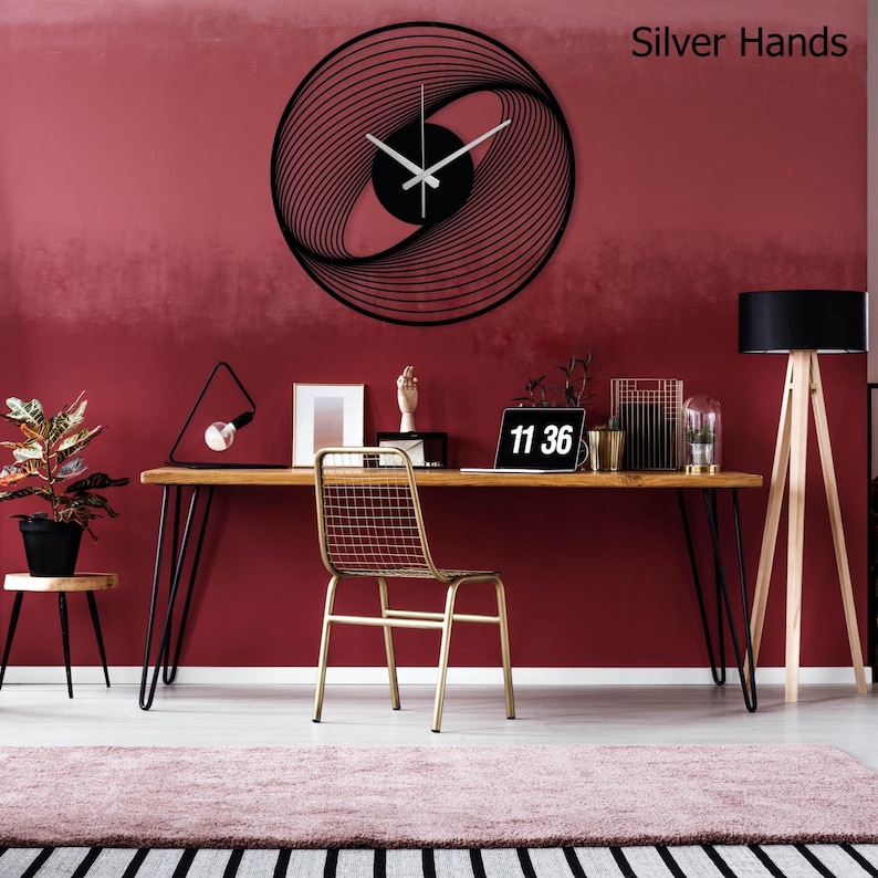 May include: A black, spiral-design wall clock with silver hands is mounted on a red wall. The clock's design features concentric lines that create a visual vortex. The time displayed on the clock is 11:36. The words "Silver Hands" are in the top right corner.