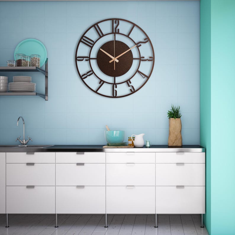 K&ouml;nnte beinhalten: Eine braune Metalluhr mit r&ouml;mischen Ziffern und schwarzem Hintergrund. Die Uhr h&auml;ngt an einer hellblauen Wand &uuml;ber einem wei&szlig;en K&uuml;chenschrank mit Schubladen.