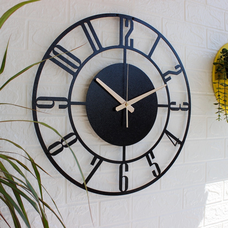 Black metal wall clock with Roman numeral markings and gold-coloured hands. The clock has a black face with a textured finish.