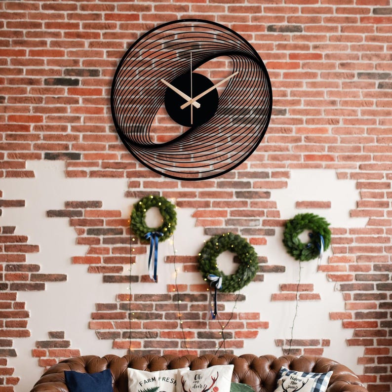 May include: Black, circular wall clock with a unique, layered design. The clock hands are light brown, and the clock is mounted on a red brick wall. The clock's design creates a spiral effect. Below the clock are three green wreaths.