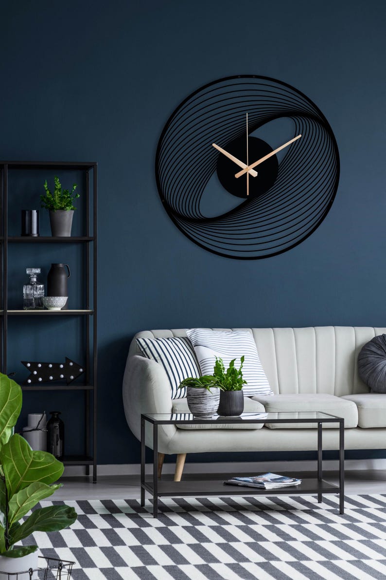 May include: A modern black wall clock with a unique, abstract design. The clock features a circular shape with a swirling pattern and gold-colored hands. It is mounted on a dark blue wall, complementing the contemporary interior decor.