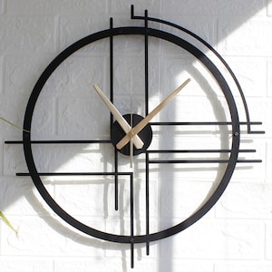 Può includere: Un orologio da parete in metallo nero con lancette dorate e un design geometrico. L'orologio ha una cornice circolare con una serie di linee che si intersecano.