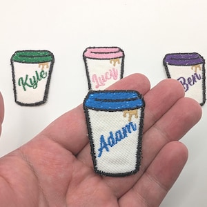 May include: Four embroidered iron-on patches shaped like coffee cups with different colored lids and names. The names are "Adam", "Ben", "Kyle", and "Lucy".