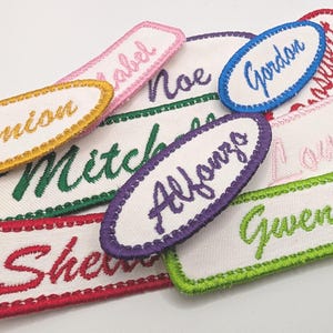 May include: A collection of colorful embroidered fabric name tags with various names including Damion, Noel, Gordon, Louisa, Gwen, Mitchell, and Alfonso.