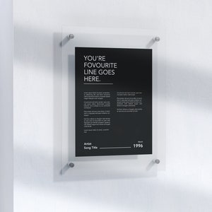 May include: A black and white poster with the text "YOU'RE FAVOURITE LINE GOES HERE."  The poster is framed in a clear acrylic frame and is hanging on a white wall.