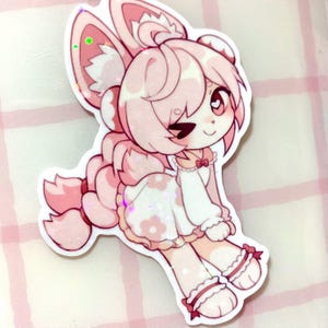 May include: A pink and white sticker of a cartoon character with bunny ears, a dress with flower details, and a long braid. The character is winking and has a heart-shaped eye. The sticker has a glittery, holographic effect.