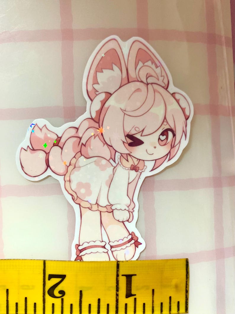 May include: A pink and white sticker of a cartoon character with large ears and a dress. The sticker is about 5 cm in height, with a glittery finish. The character is winking. The sticker is on a pink and white checkered background.