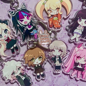 Puede incluir: Una colección de llaveros de acrílico transparente con personajes de anime estilo chibi con cabello y atuendos coloridos. Cada dije incluye un anillo y un cierre de metal. Una pequeña etiqueta circular muestra el texto Cinna bunny cream ETSY.COM.