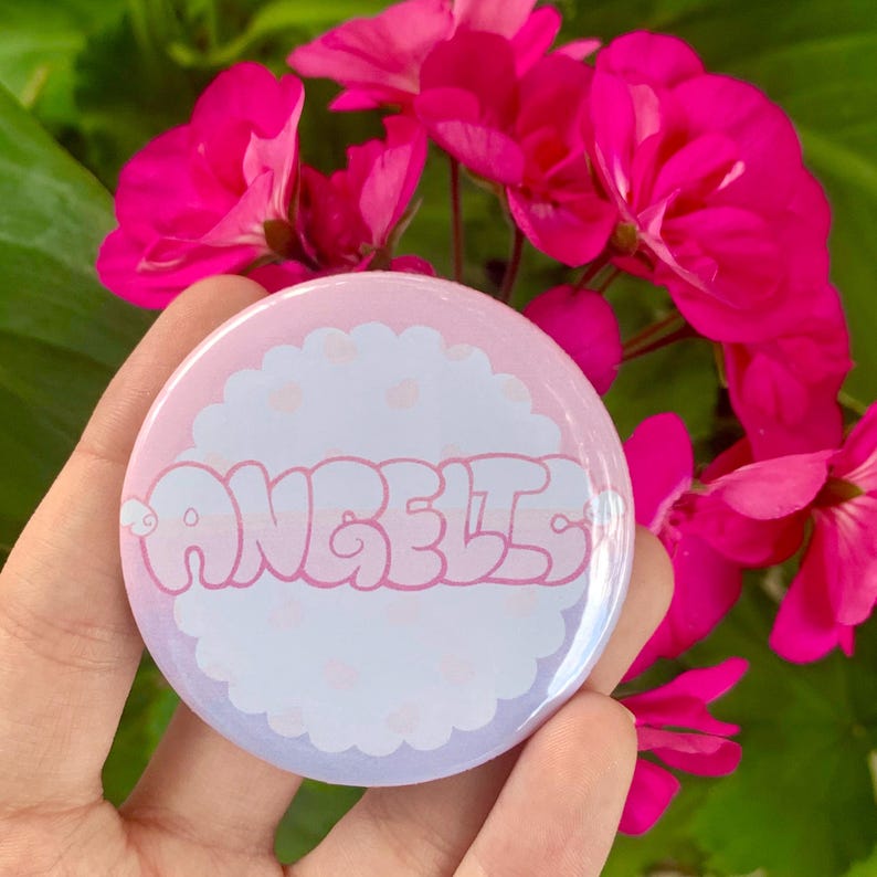 May include: A pink and purple button with a white cloud design and the word "ANGELIC" in pink bubble letters.