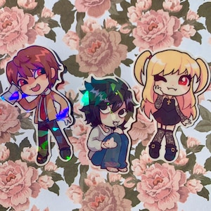 Peut inclure: Trois autocollants holographiques représentant des personnages d'anime. Les personnages sont Light Yagami, L et Misa Amane de l'anime Death Note. Les autocollants sont sur un fond floral.