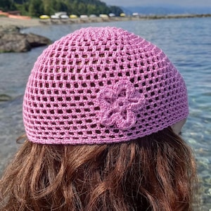 May include: Pink crocheted hat with a flower design. The hat is made with a mesh pattern.