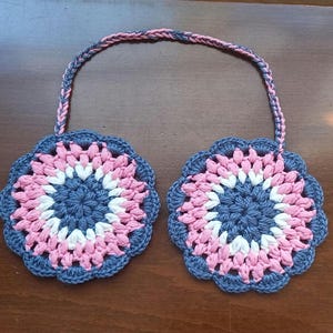 May include: Crocheted ear warmers in a floral pattern. The ear covers are blue, pink, and white, joined by a braided strap. These ear warmers are made of soft yarn and are designed to keep ears warm in cold weather.