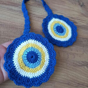 Op de afbeelding: Twee ronde gehaakte ornamenten met een concentrisch patroon van donkerblauw, lichtblauw, geel en wit garen. De stukken zijn verbonden door een gehaakte band, waarbij elk rond element is afgewerkt met een geschulpte rand.