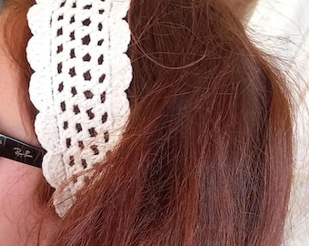 May include: A wide, off-white crochet headband featuring an intricate openwork pattern and a scalloped edge. The accessory is crafted with a textured yarn construction, showcasing a repeating geometric design that spans the width of the band.