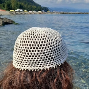 May include: A white crocheted hat with a beaded trim. The hat is made of a fine mesh material and has a rounded shape.