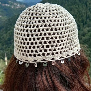 May include: A white crocheted hat with a scalloped edge and silver sequins around the brim.