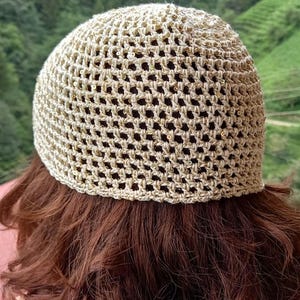 May include: A beige crochet hat with gold sequins. The hat is made with a mesh pattern and has a rounded crown.