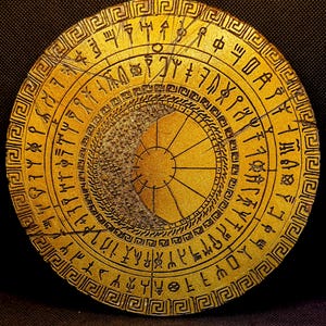 Puede incluir: Un artefacto circular de color dorado con símbolos y patrones grabados. El diseño presenta círculos concéntricos con un patrón central de rayos de sol y un borde de formas geométricas repetidas. La superficie tiene una apariencia desgastada.