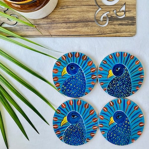 Könnte beinhalten: Set aus vier runden Holz-Untersetzern mit bemalten Pfauenmotiven. Jeder Untersetzer zeigt einen blauen Pfau mit gelbem Schnabel und orangefarbenen Akzenten auf blauem Hintergrund.